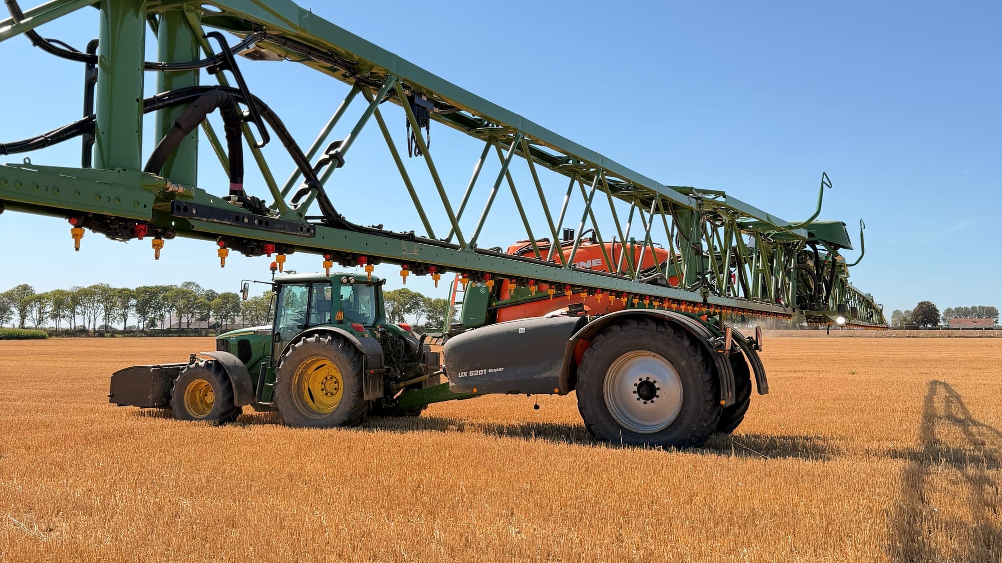 A tractor with an unfolded field sprayer on a stubble field.