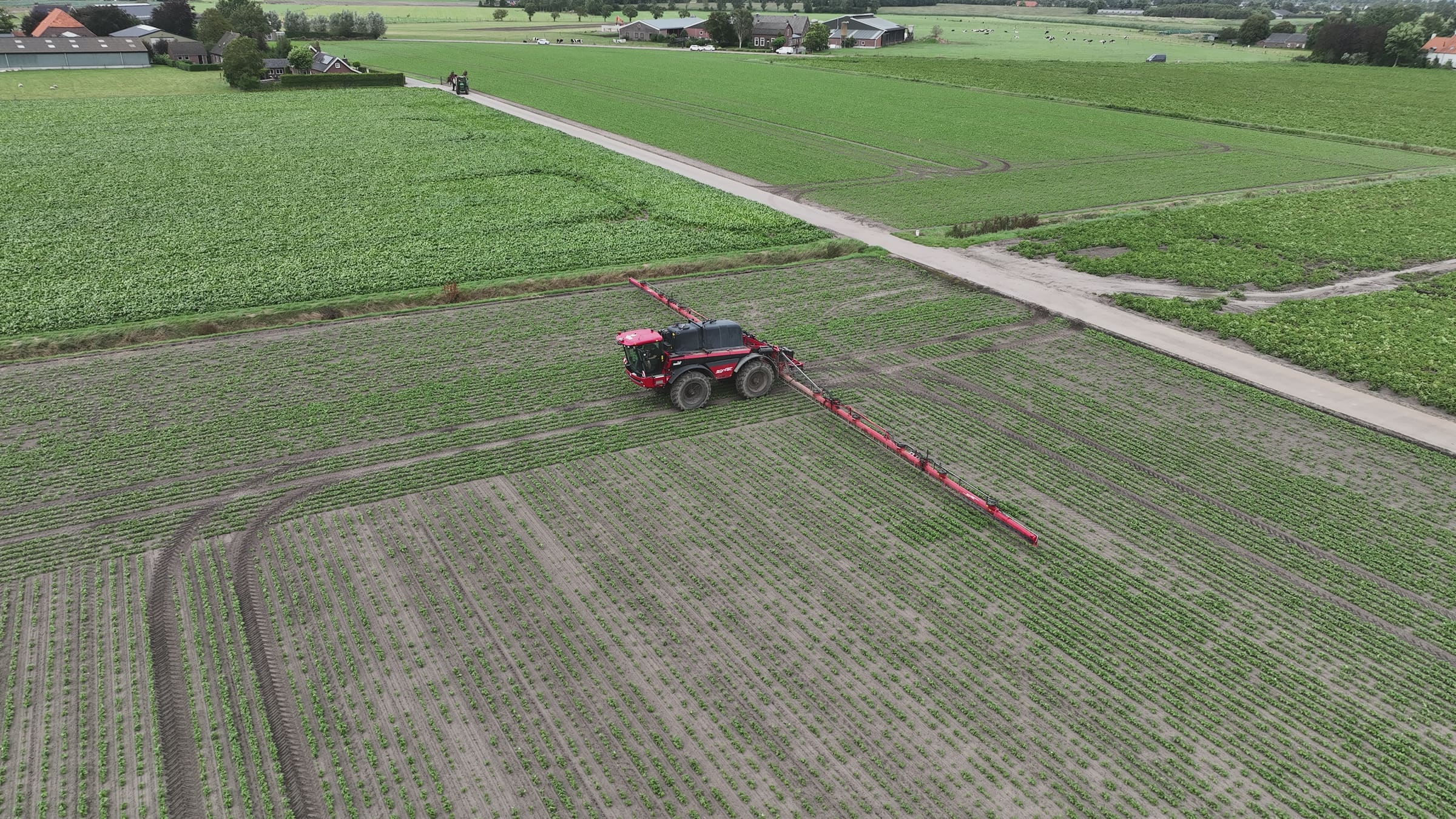Rode veldspuit rijdt door een perceel, gezien vanuit de drone